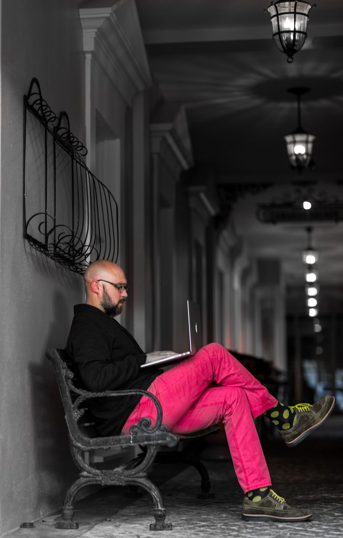 James Hanratty on a bench with a laptop, in pink pants and polka-dot socks